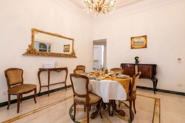 A dining room with a round table, chairs, a chandelier, a mirror, and a framed picture on the wall.