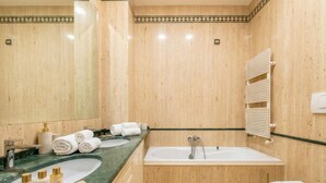 A bathroom with a large mirror, two sinks, a bathtub, and a toilet.