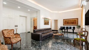 A spacious lobby with a black leather sofa, a patterned armchair, a piano, and a dining table with chairs. - The One - Luxury Apartment with Piano (Bari)