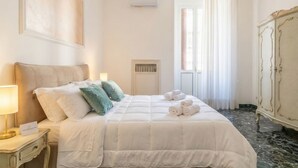 A hotel room with a bed, a nightstand with a lamp, a radiator, a wardrobe, and a window with curtains.