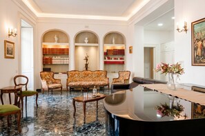 Uma sala de estar ampla com piso de mármore, um piano de cauda e uma estante com livros e objetos decorativos.