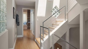 A modern interior with a staircase, wooden flooring, and a hallway leading to a room with a window and a door.