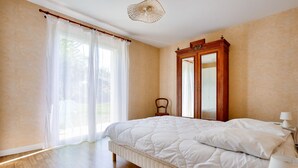 A bedroom with a large bed, wooden floor, a mirror, and a window with curtains. - Spacious house for 4 with garden and terrace (Pleurtuit)