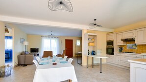 A modern kitchen with white cabinets, a dining area with a table set for four, and a living room with a sofa and TV. - Spacious house for 4 with garden and terrace (Pleurtuit)