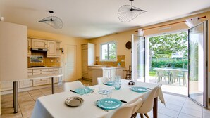 A dining area with a table set for four, a kitchen with white cabinets, and a view of the garden through the sliding glass door. - Spacious house for 4 with garden and terrace (Pleurtuit)