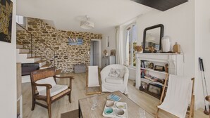 Un salon chaleureux avec un mur en pierre, une cheminée, une bibliothèque et un coin repas avec une table mise pour deux personnes.