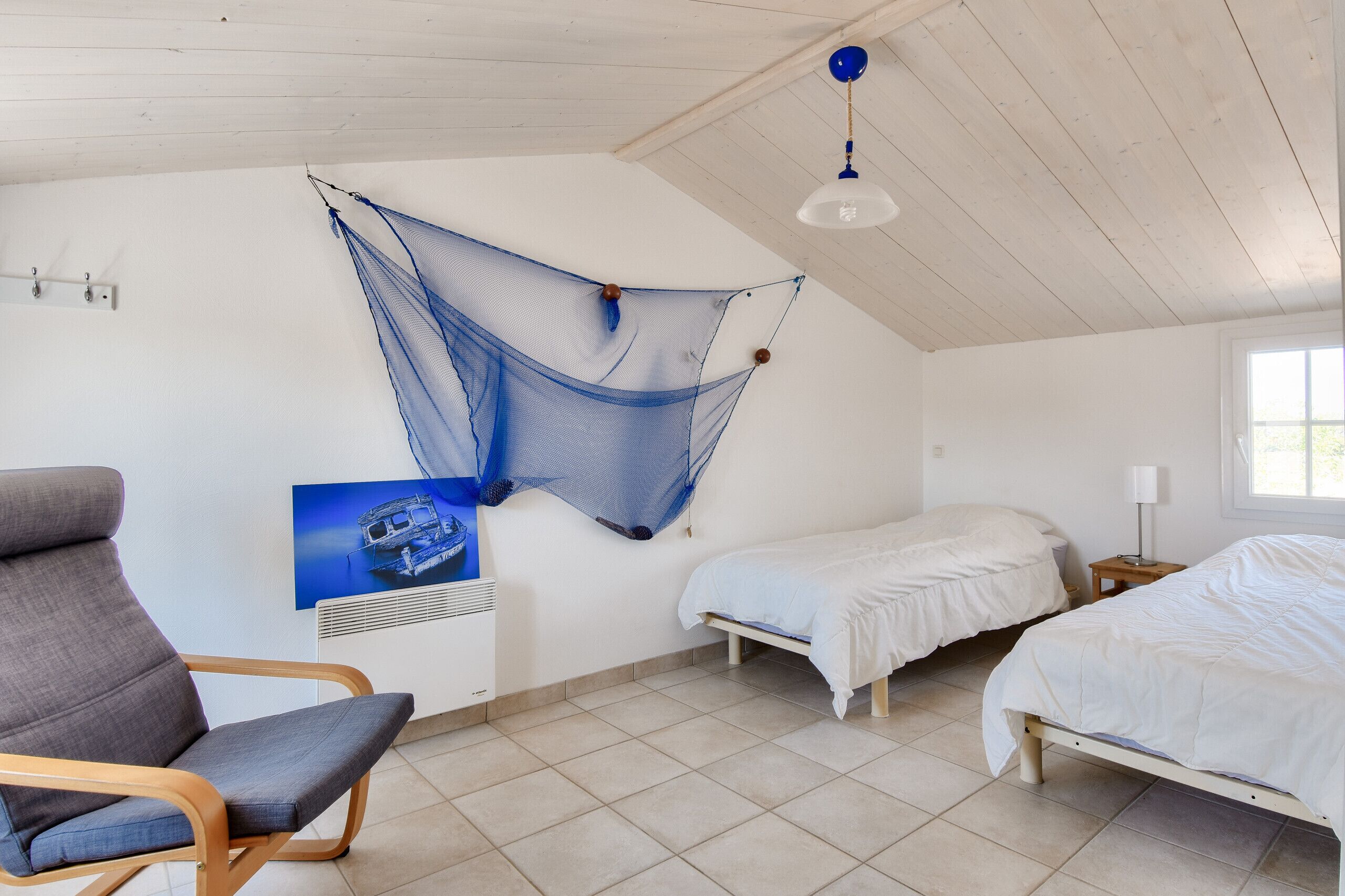 A room with a hammock, two beds, a chair, and a poster on the wall.