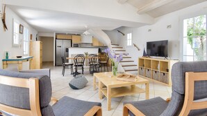 A spacious living area with a wooden coffee table, grey upholstered chairs, a television, and a kitchen in the background. - 500 m from the beach - House for 6 - Terrace (L'Epine)