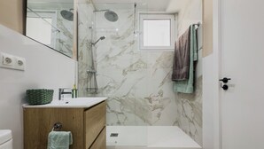 Un baño moderno con cabina de ducha de vidrio, tocador de madera con lavamanos y un inodoro.