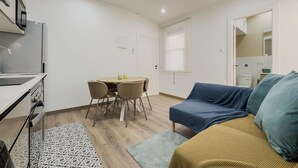 En kompakt opholdsstue med tekøkken, spiseplads og sofa.