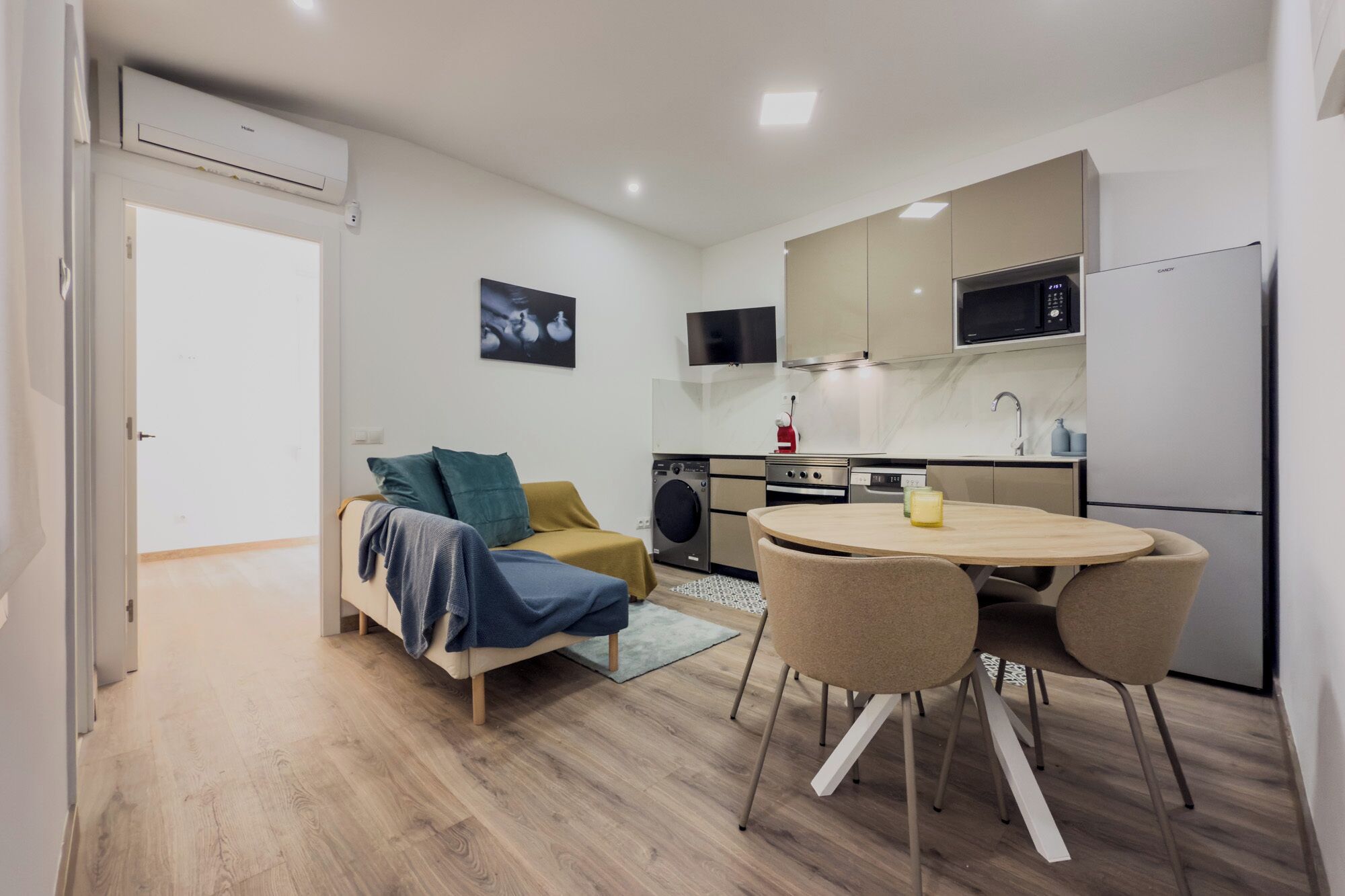 Un espace de vie compact comprenant un canapé, une table à manger avec des chaises, un coin cuisine équipé d’un four à micro-ondes et d’un four traditionnel, ainsi qu’un lave-linge.