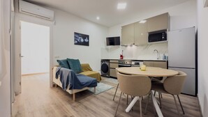 Un espacio habitable compacto con sofá, una mesa de comedor con sillas, una zona de cocina con microondas y horno, y una lavadora.