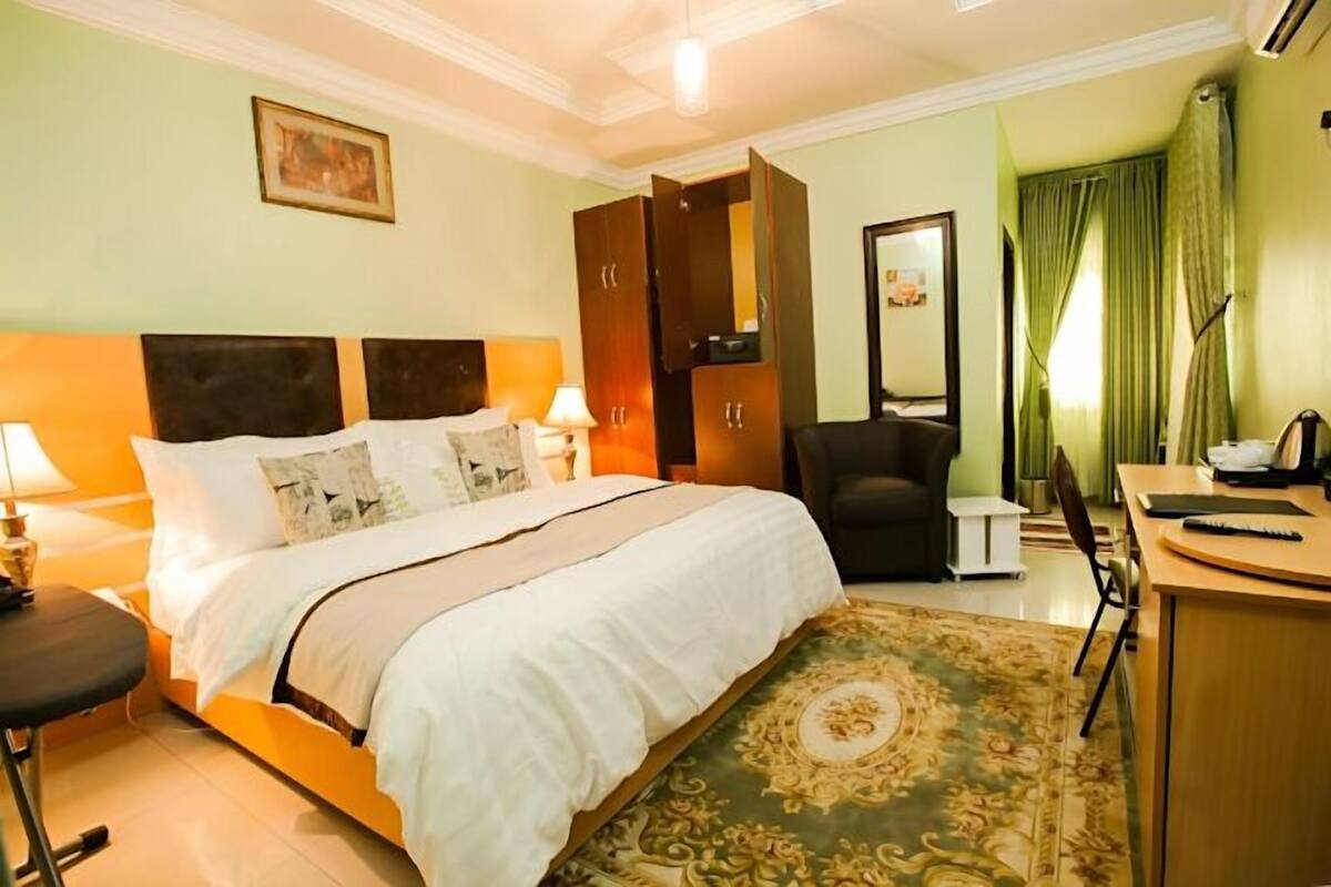 A hotel room with a bed, bedside lamps, a desk with a chair, a mirror, and a green curtain.