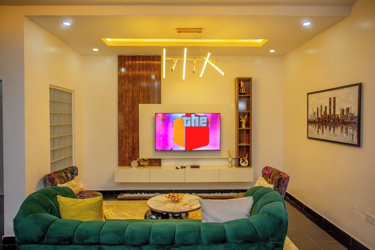 A modern living room with a green sofa, a TV mounted on the wall, and a cityscape painting.