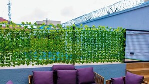 Ein Außenbereich mit Sitzgelegenheiten, darunter eine Couch und Stühle, einem Tisch mit Glasplatte und einem grünen Kunstrasen.