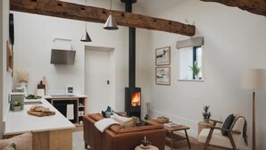 A modern living room with a fireplace, a sofa, a coffee table, and a dining area. - Longstones Avebury – Ridgeway (Marlborough)