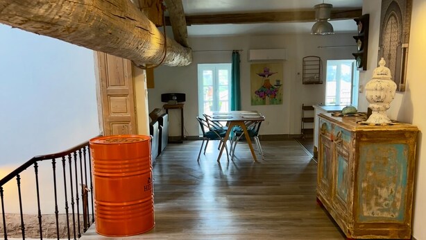 A spacious room with wooden beams, a dining table with chairs, a large orange barrel, and a vintage cabinet. - Quality LOFT for 4 people (Lamalou-les-Bains)