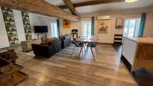 A spacious living area with wooden flooring, a sofa, a dining table with chairs, and a kitchen area with a countertop and cabinets. - Quality LOFT for 4 people (Lamalou-les-Bains)