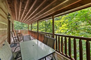 A covered outdoor area with a table and chairs, surrounded by a wooden railing, overlooking a forested area. - Peaceful 2BR w/Hot Tub*Game Room*Jacuzzi*Privacy! (Sevierville)