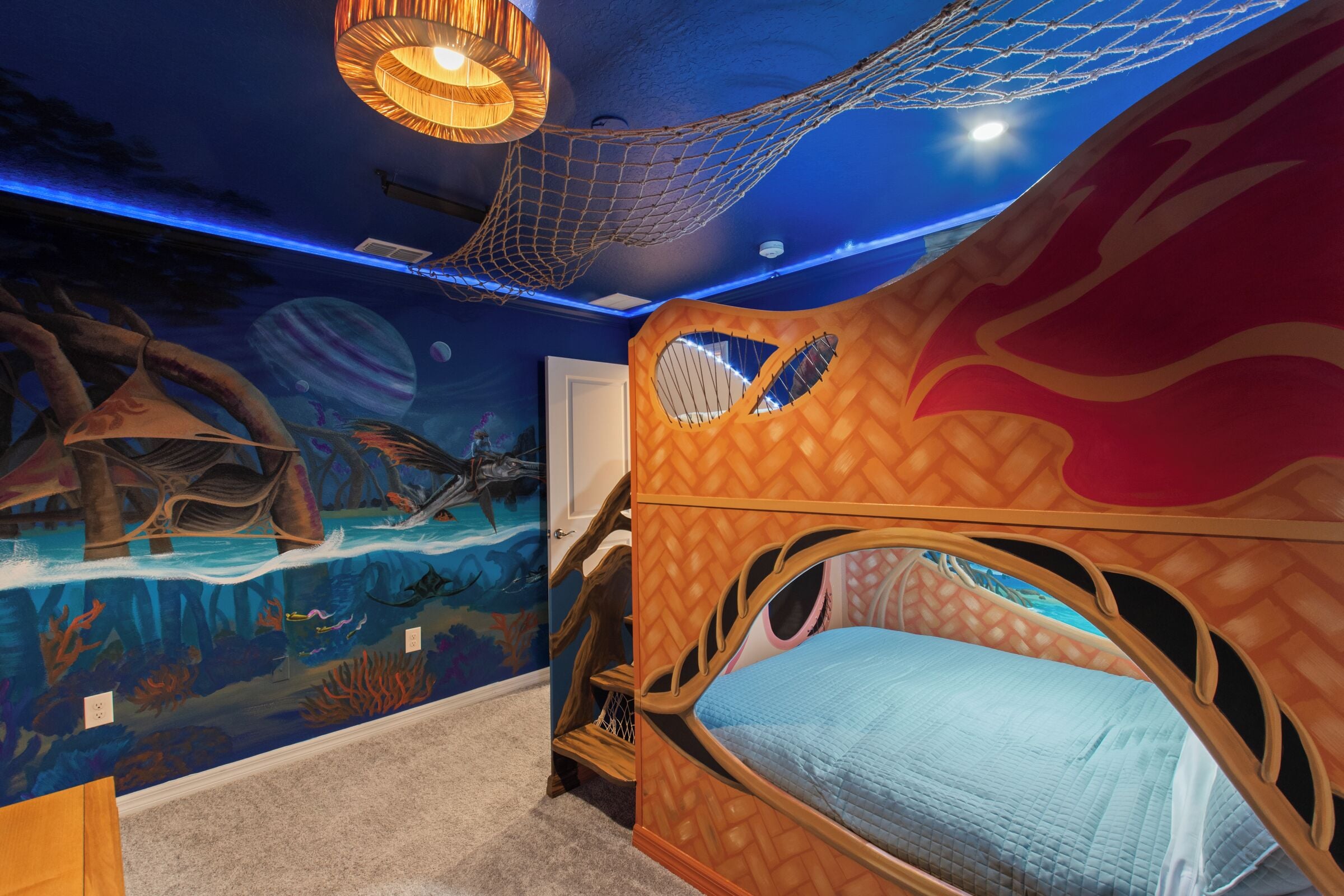 Un dormitorio infantil con una cama, un mural de una escena submarina y una red en el techo.