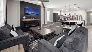 A modern living room with a flat-screen TV, grey sofas, a wooden coffee table, and a fireplace.