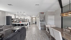 A modern kitchen with a central island, a dining area with a long table and chairs, and a staircase leading to an upper level.