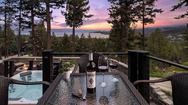 A glass table with a bottle of Coppola wine, two wine glasses, and a corkscrew on a balcony overlooking a scenic view of trees and a sunset.