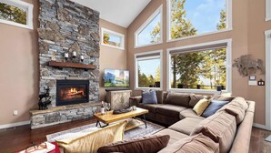 A living room with a stone fireplace, large windows, and a cozy sectional sofa.