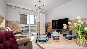 A modern living room with a sofa, a dining table set with blue plates, a TV, and a fan. - Apartamenty Sun&Snow Platinum Towers (Warsaw)