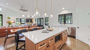 A modern kitchen with a large island, wooden cabinets, and pendant lighting.