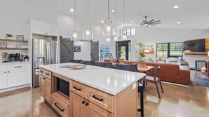 A modern kitchen with a large island, wooden cabinets, and pendant lighting.