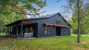 A modern, dark-colored cabin with a covered porch and a large window.