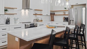 A modern kitchen with white cabinetry, stainless steel appliances, and a central island with bar stools.