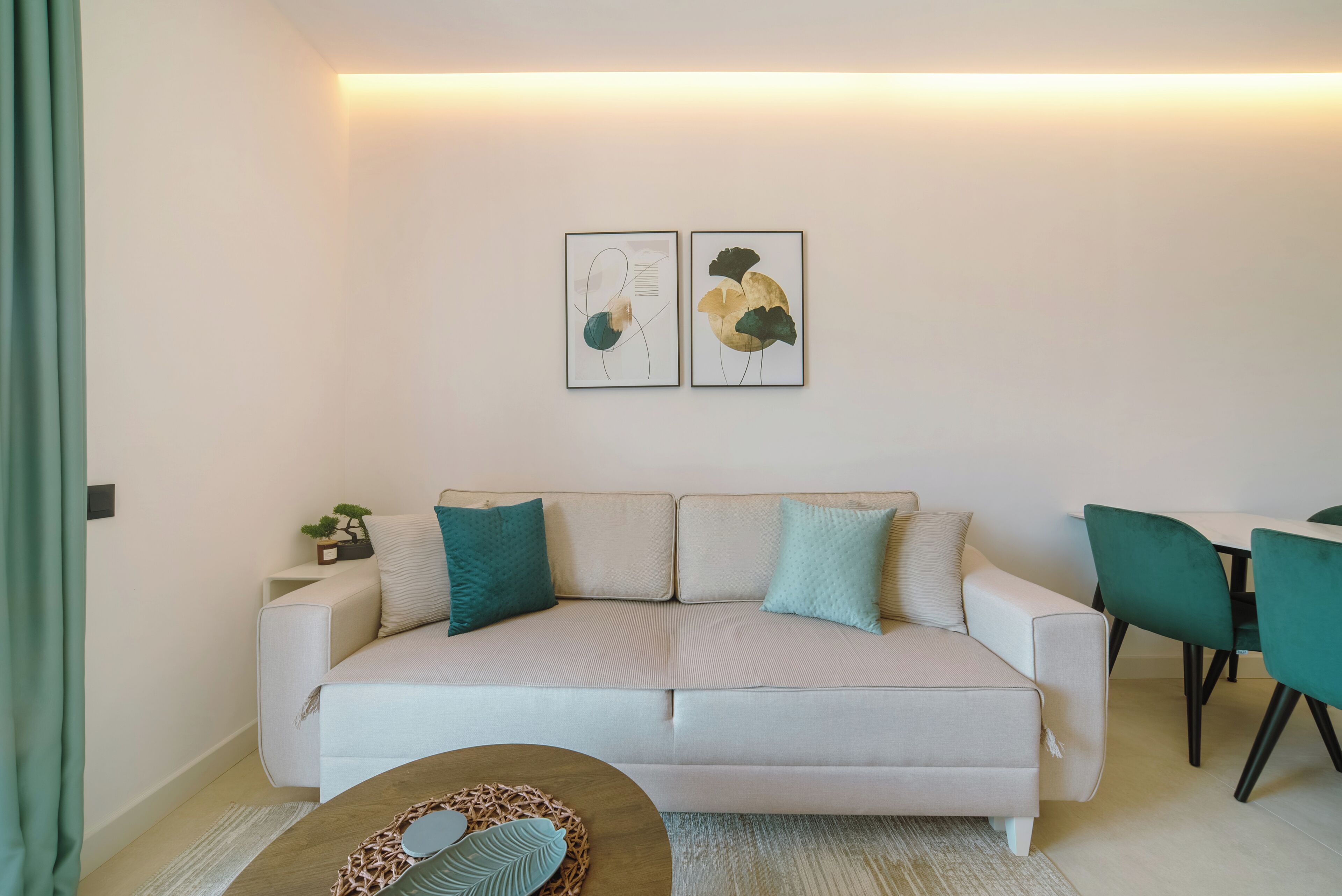 Una sala de estar moderna con un sofá color beige, cojines color turquesa y dos obras de arte abstracto en la pared.