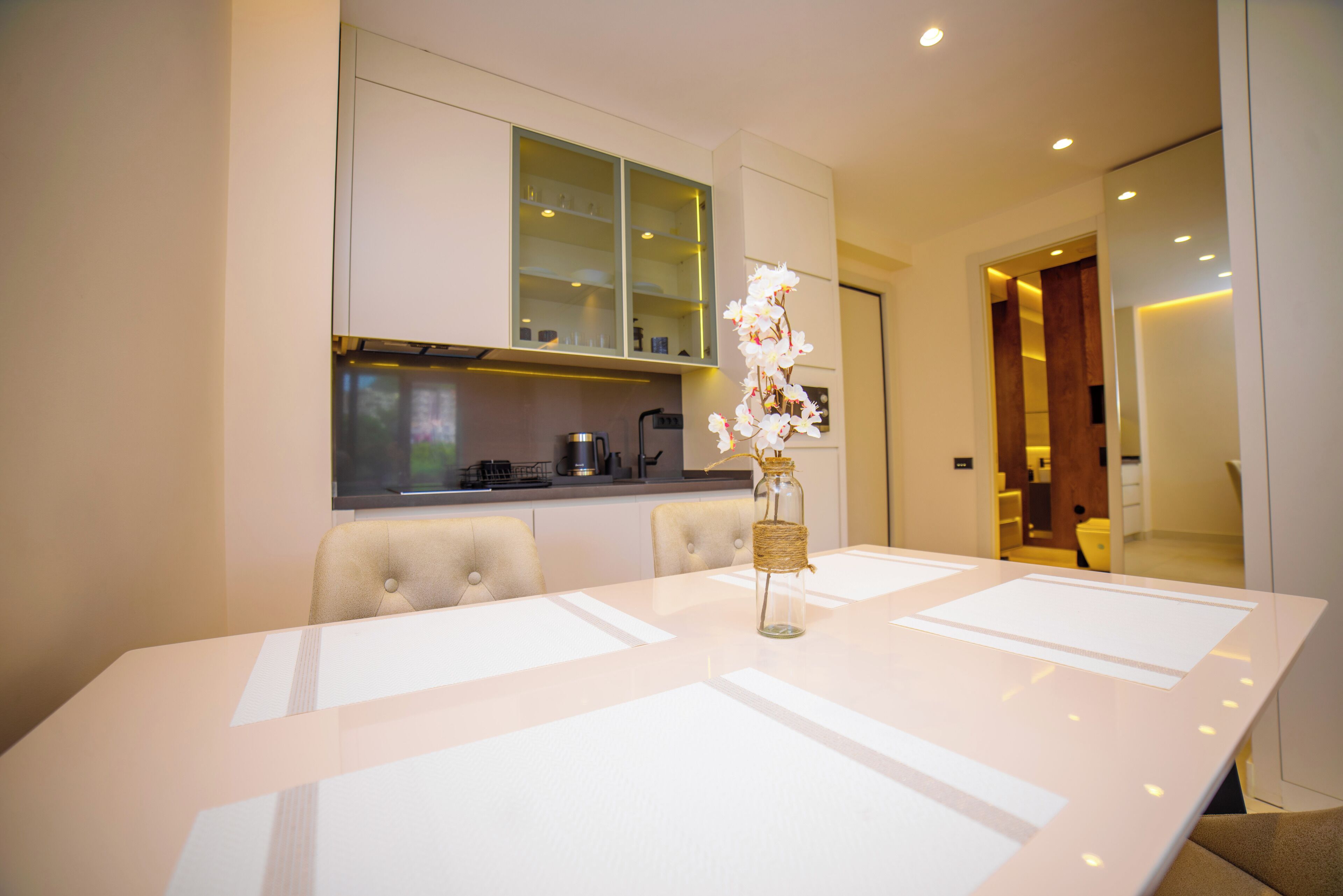 Un comedor moderno con una mesa blanca, sillas acolchadas y un jarrón decorativo.