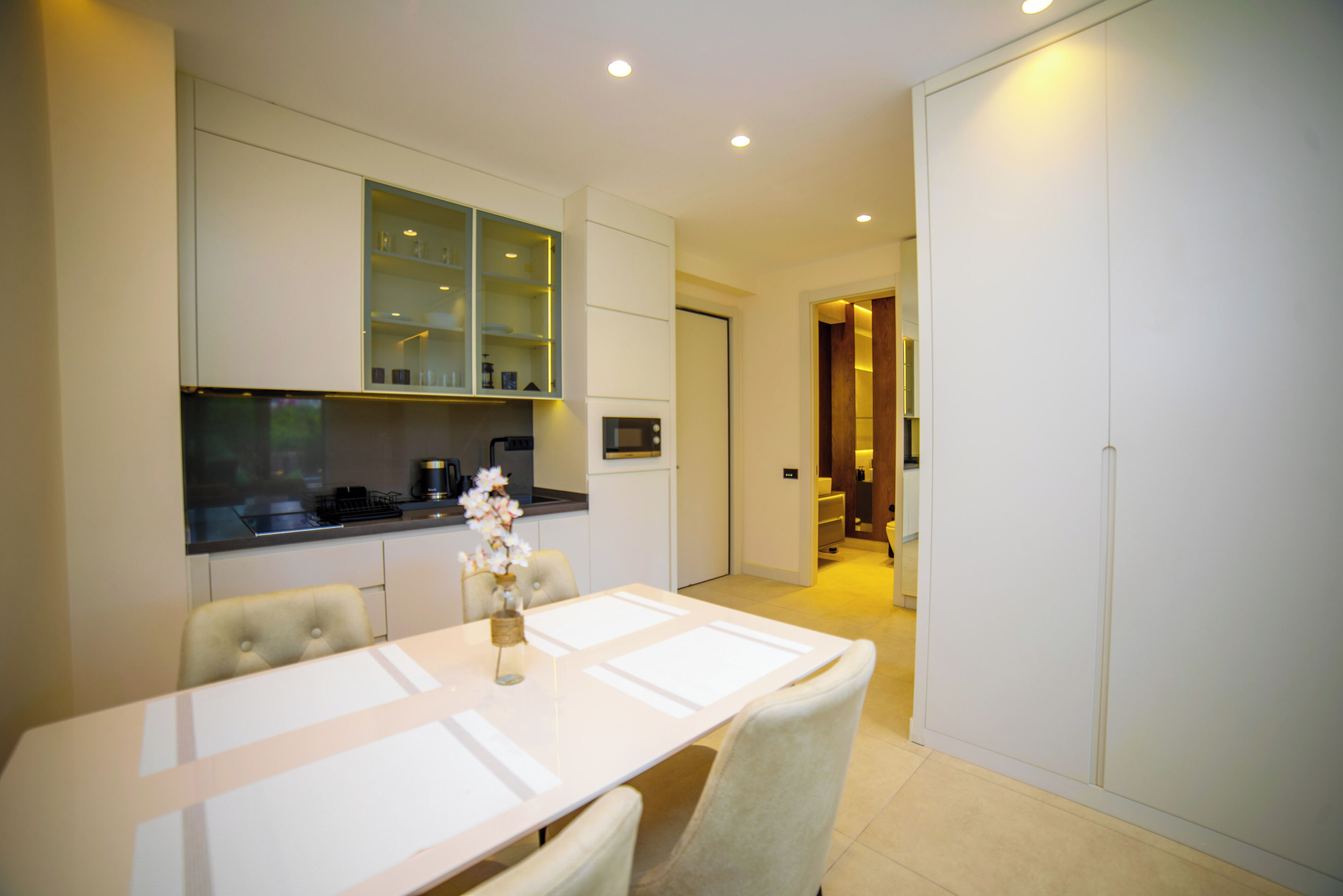 A modern kitchen with white cabinetry, a dining table with chairs, and a vase with flowers.