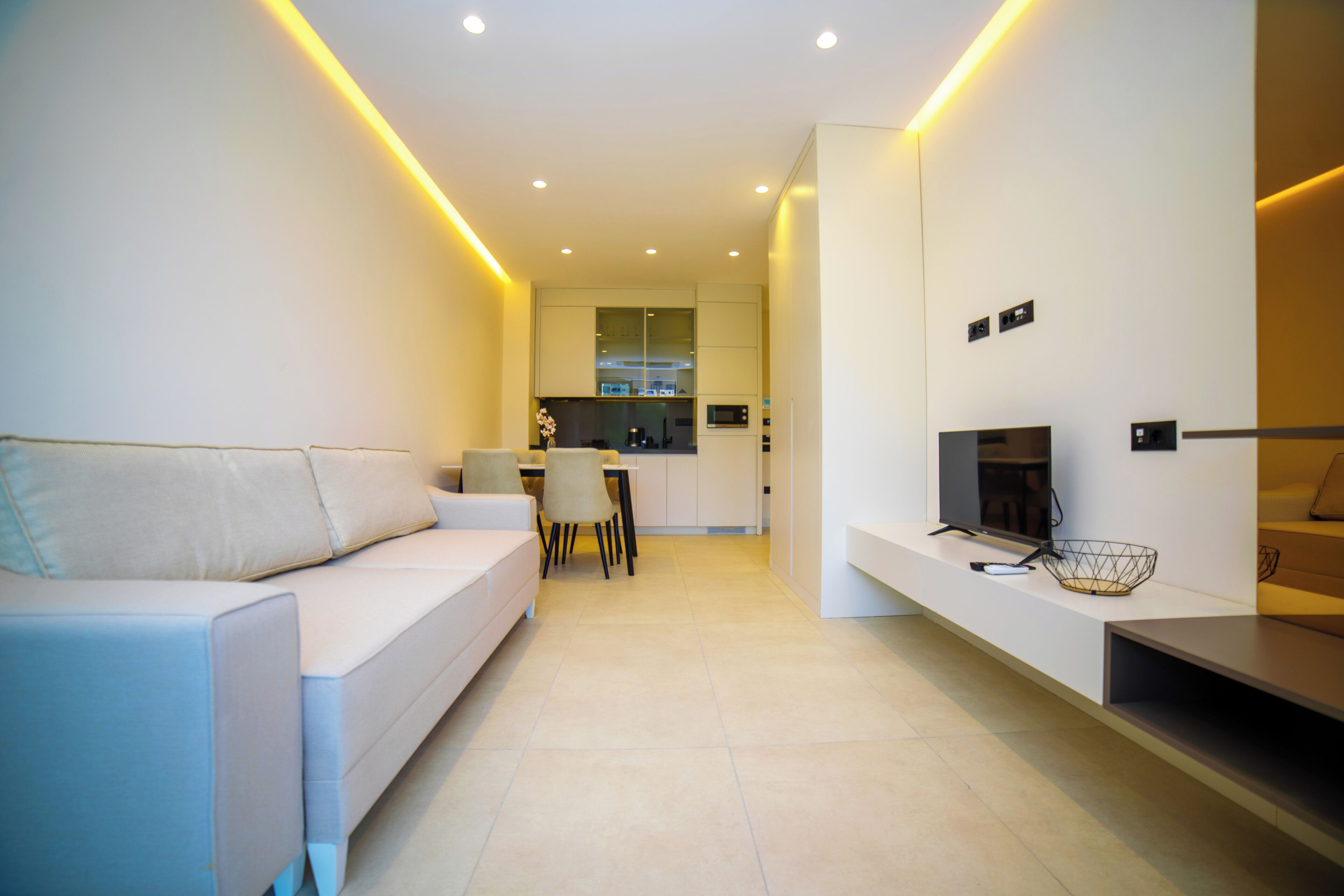 A modern living room with a sofa, a TV, and a kitchen in the background.