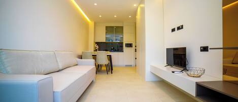 A modern living room with a sofa, a TV, and a kitchen in the background.