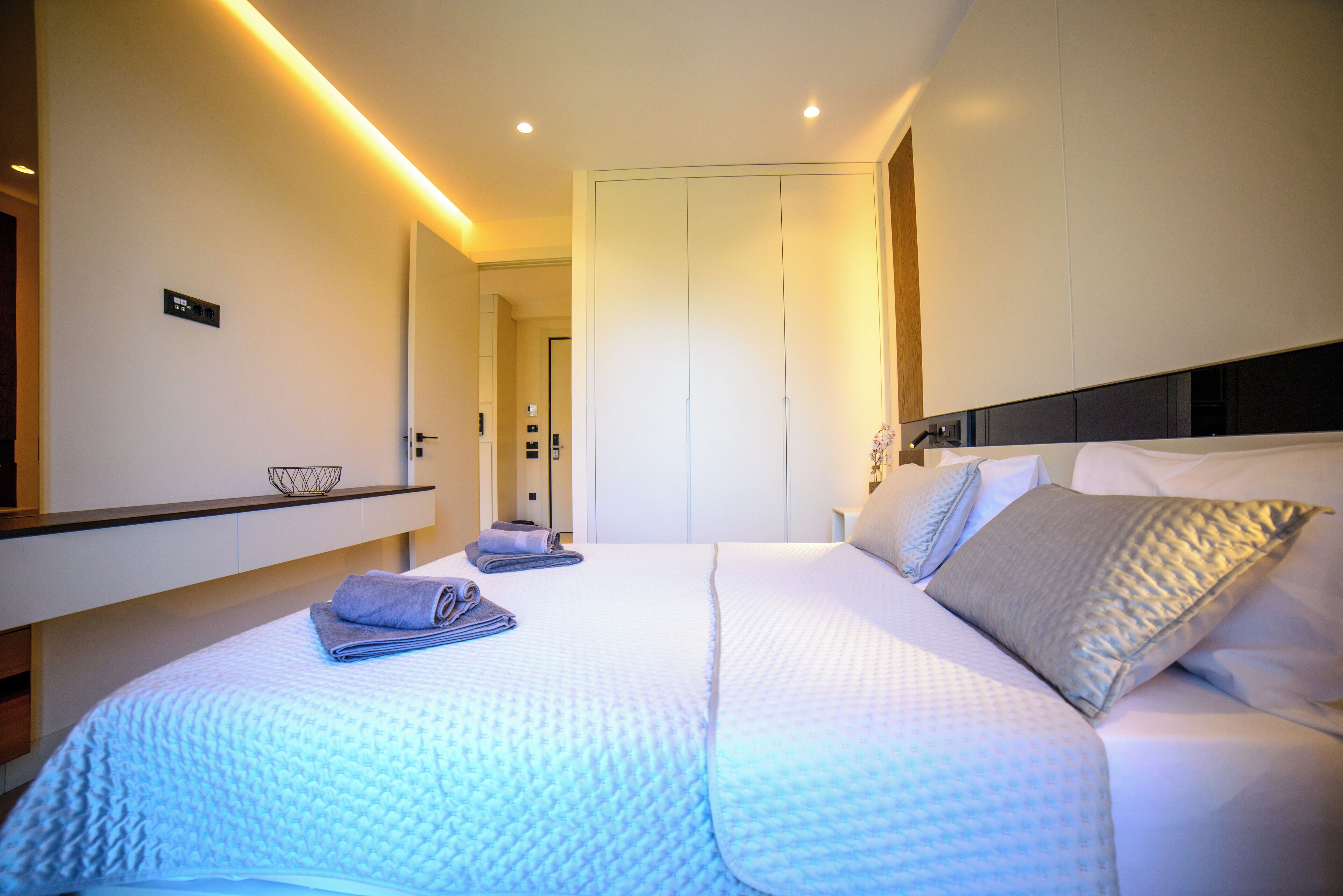 A modern hotel room with a neatly made bed, a bedside table with a lamp, and a large wardrobe.