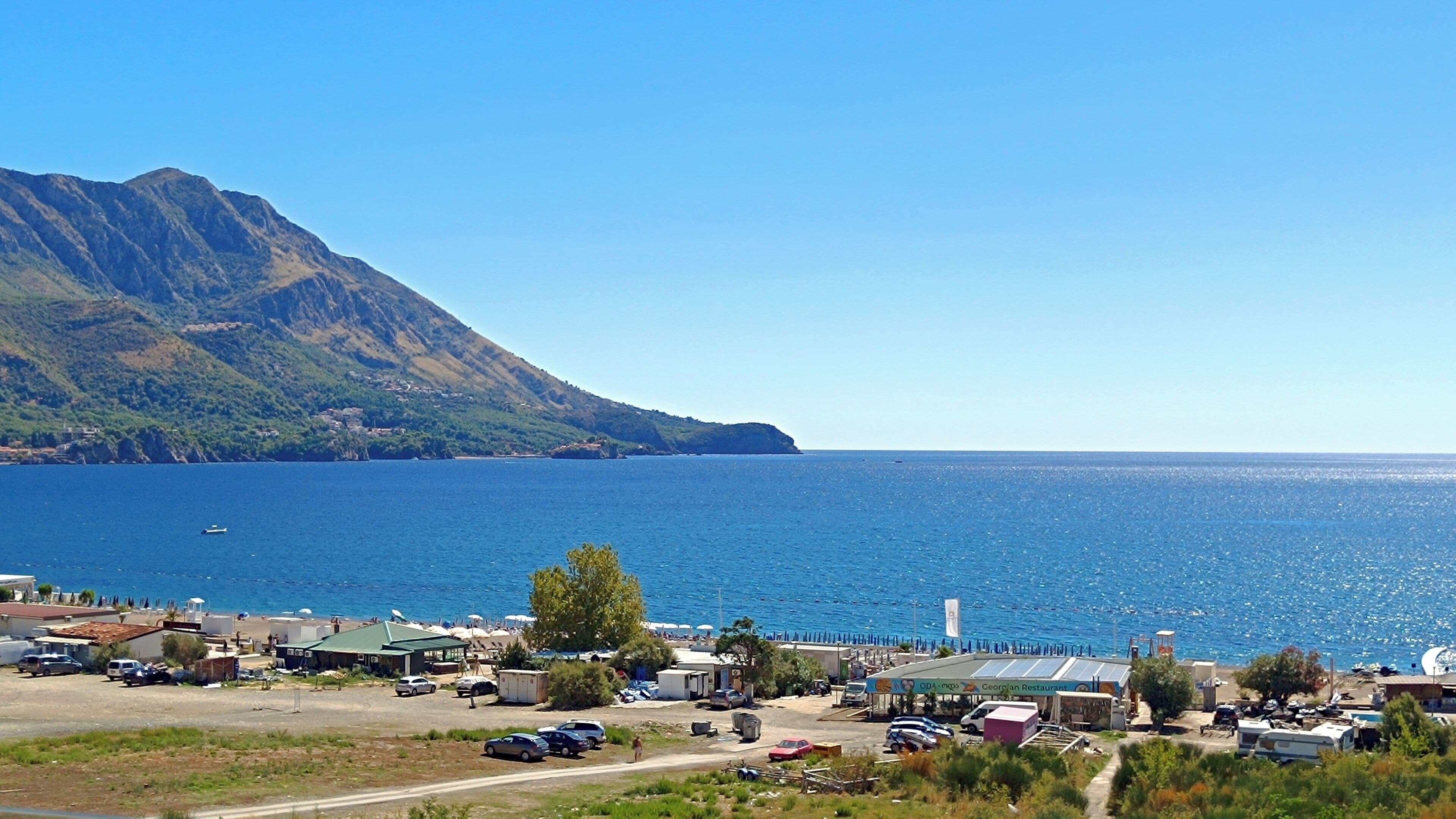 Une zone côtière avec une montagne en arrière-plan, une marina avec des bateaux et un restaurant appelé « Georgian Restaurant ».