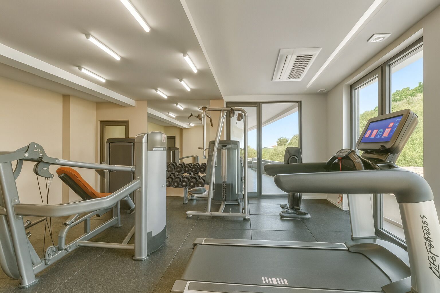 Une salle de sport équipée de matériel d’exercice, d’un tapis de course et d’un écran numérique.