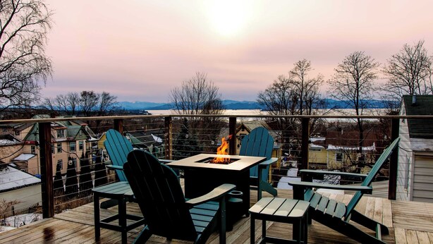 A deck with outdoor seating, a fire pit, and a view of a snowy landscape. - Large Private 2 Bedroom Apt w/ Epic Deck View (Burlington)