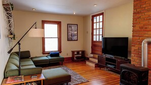 A living room with a sectional sofa, a television, a fireplace, and a bookshelf. - Large Private 2 Bedroom Apt w/ Epic Deck View (Burlington)