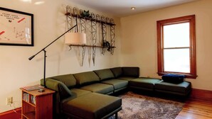 A modern living room with a sectional sofa, a small wooden side table, a floor lamp, and a large window. - Large Private 2 Bedroom Apt w/ Epic Deck View (Burlington)