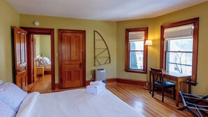 A hotel room with a bed, a desk, and a chair. There is a window with a view of trees and a lamp on the desk. - Large Private 2 Bedroom Apt w/ Epic Deck View (Burlington)