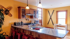 A kitchen with a central island, red bar stools, wooden cabinets, and pendant lighting. - Large Private 2 Bedroom Apt w/ Epic Deck View (Burlington)