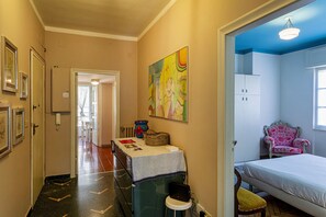 A hotel room with a bed, a chair, a table with a tablecloth, a painting on the wall, and a window with curtains.