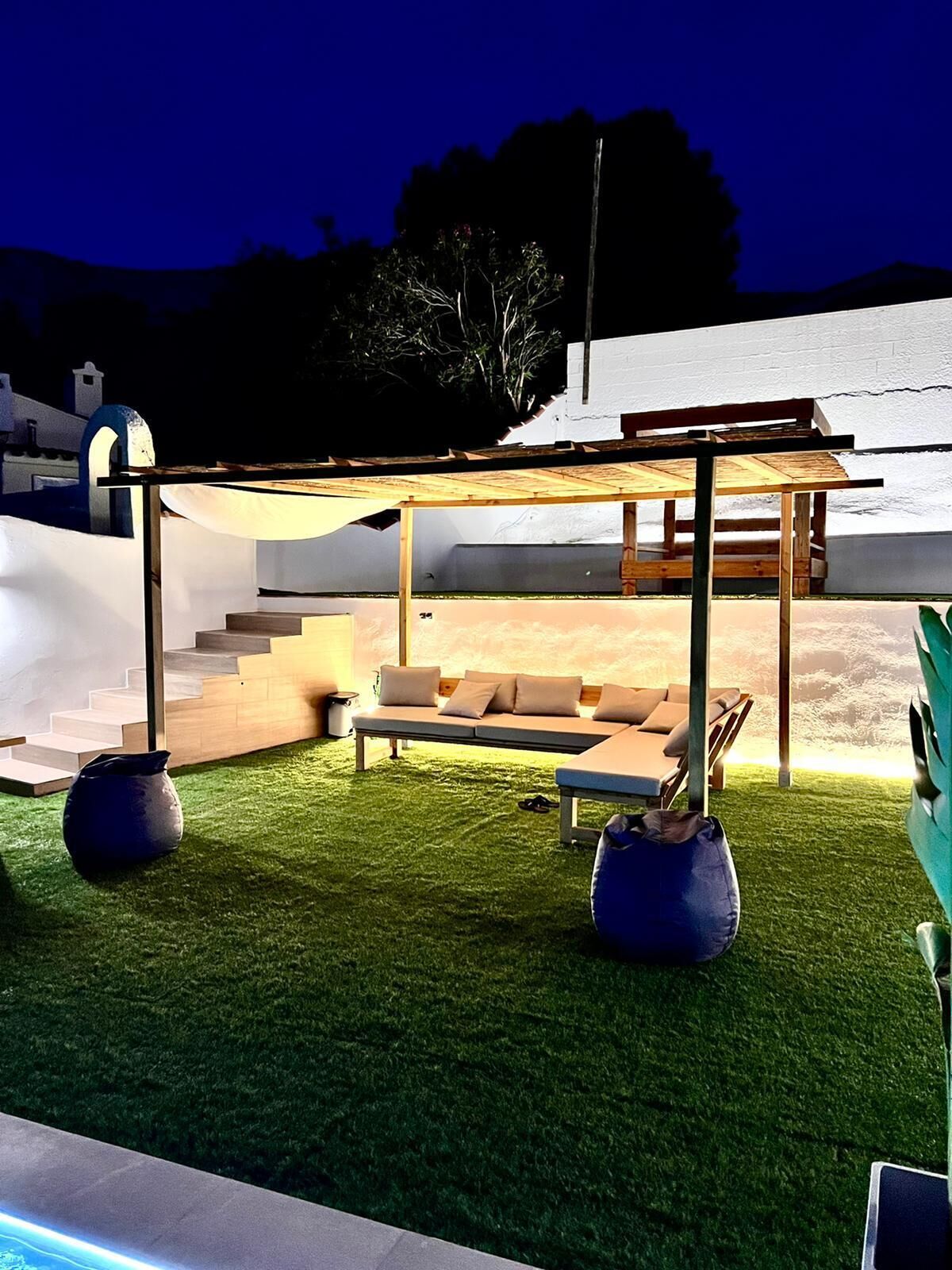 Un espace de vie extérieur moderne, agrémenté d’une pergola en bois, d’un canapé et de deux grands bacs à plantes.