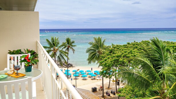 Een balkon met uitzicht op een strand, palmbomen en een heldere lucht.