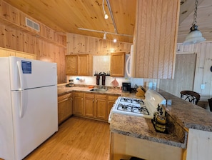 Fully equipped kitchen with a refrigerator, gas stove, sink, and hanging light fixture.
